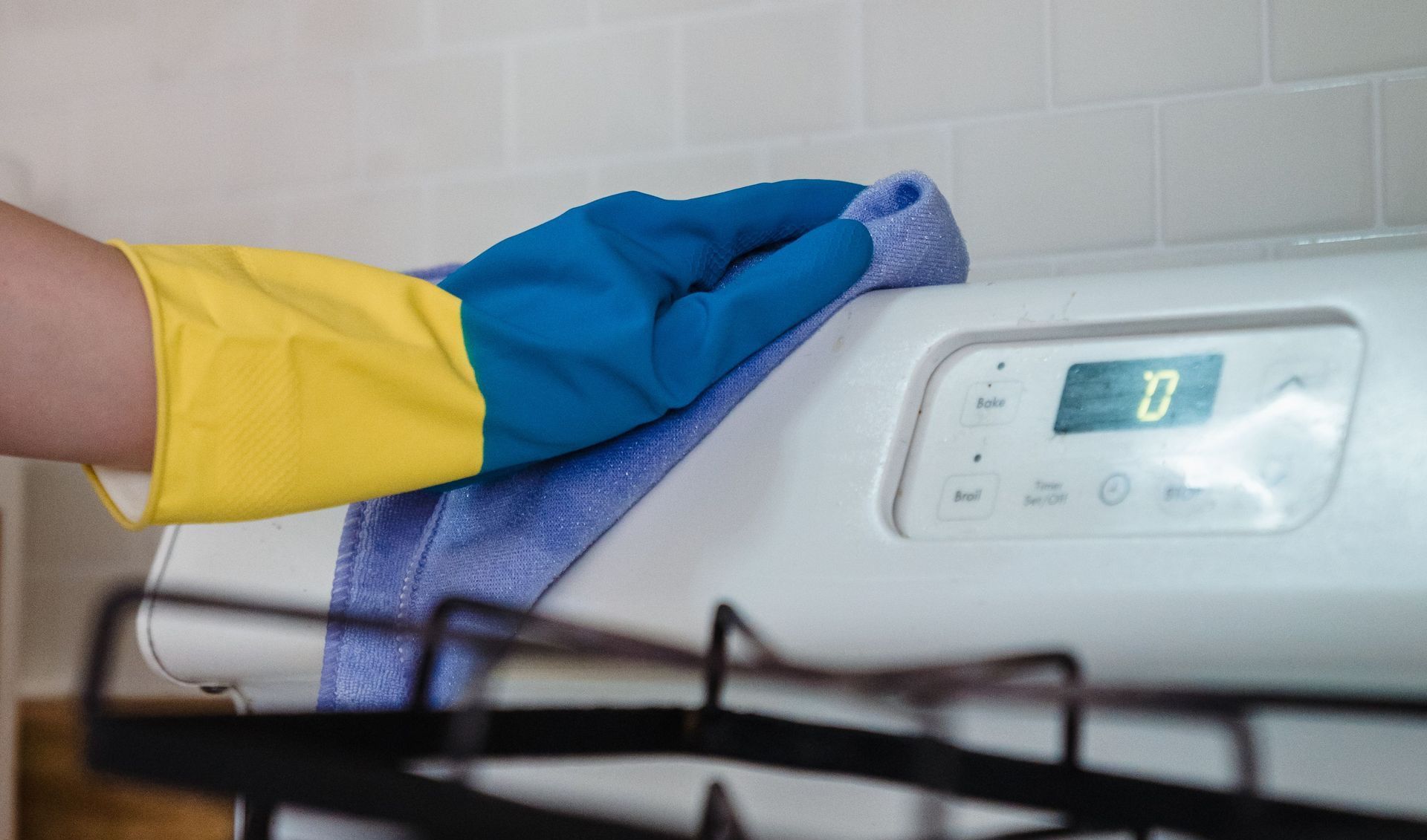 A person wearing rubber gloves cleans the kitchen stove with a cloth, emphasizing hygiene and household chores.